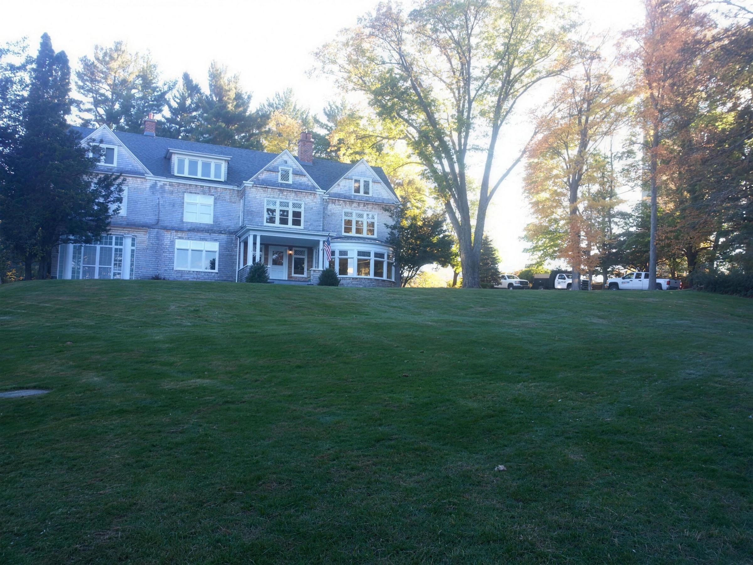 Sweeping estate lawn rising toward a shingle-style house among mature trees